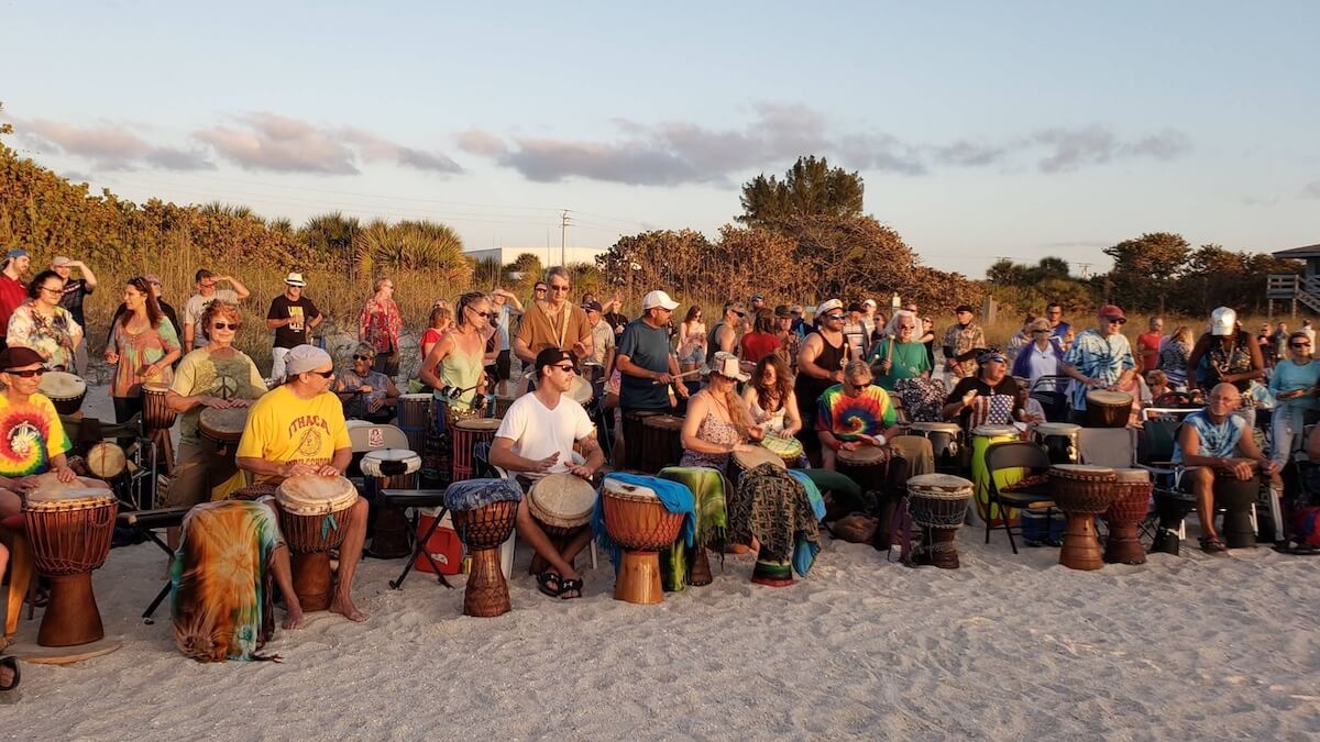 Dozens of drummers playing djembes on the sand at the Nokomis Beach drum circle near sunset